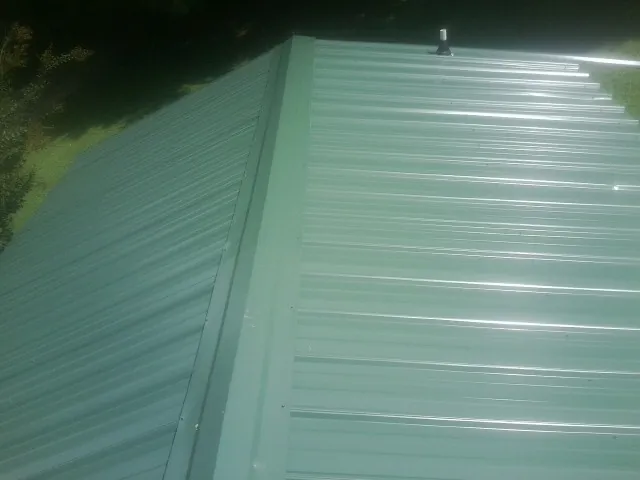 New green metal panels meeting at the ridge of a roof — Flat Roof Repair work by our crew in Marcellus