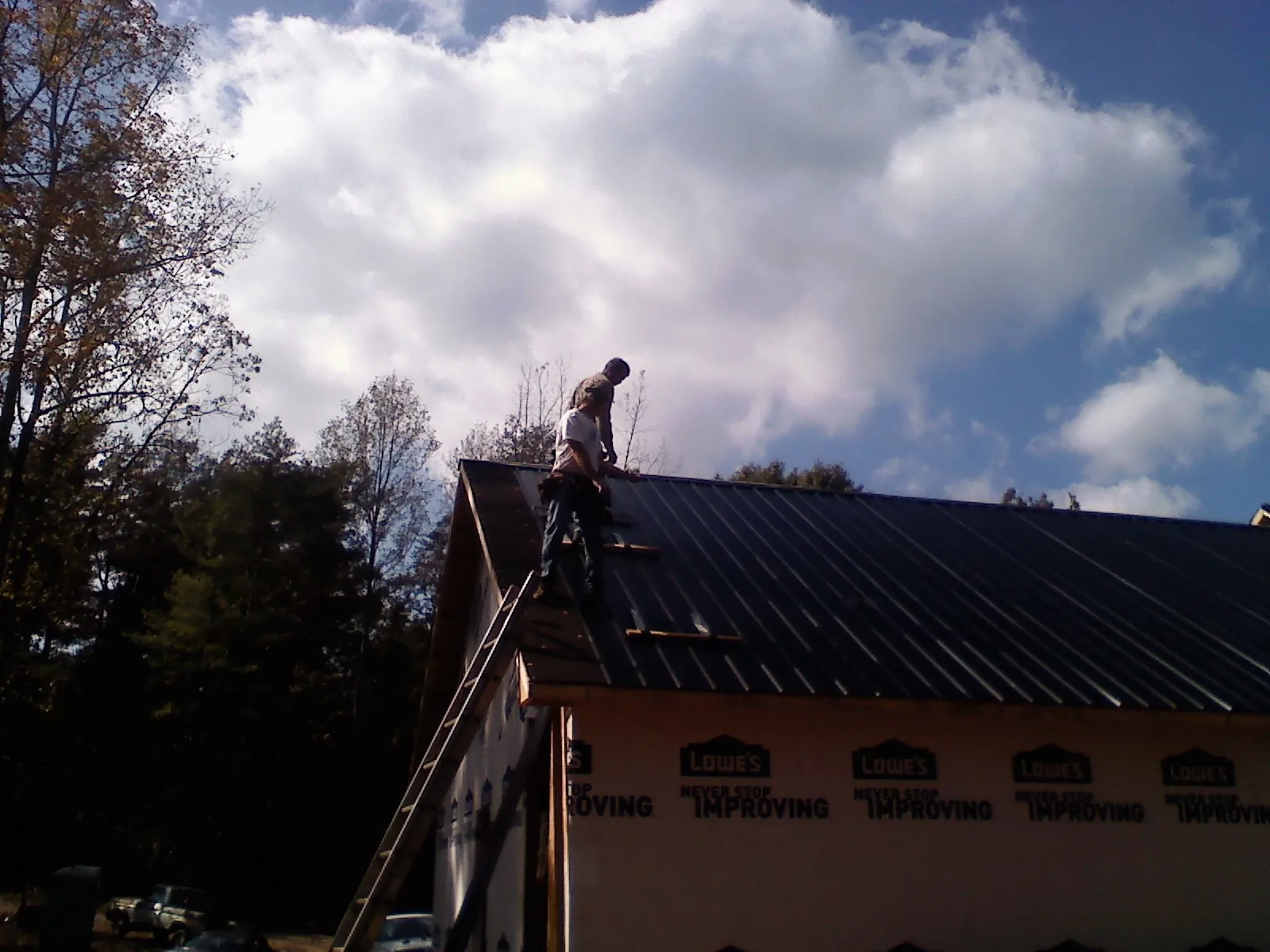 Roofer fastening dark metal panels high against a cloudy sky, from a Roof Inspection job in Marcellus