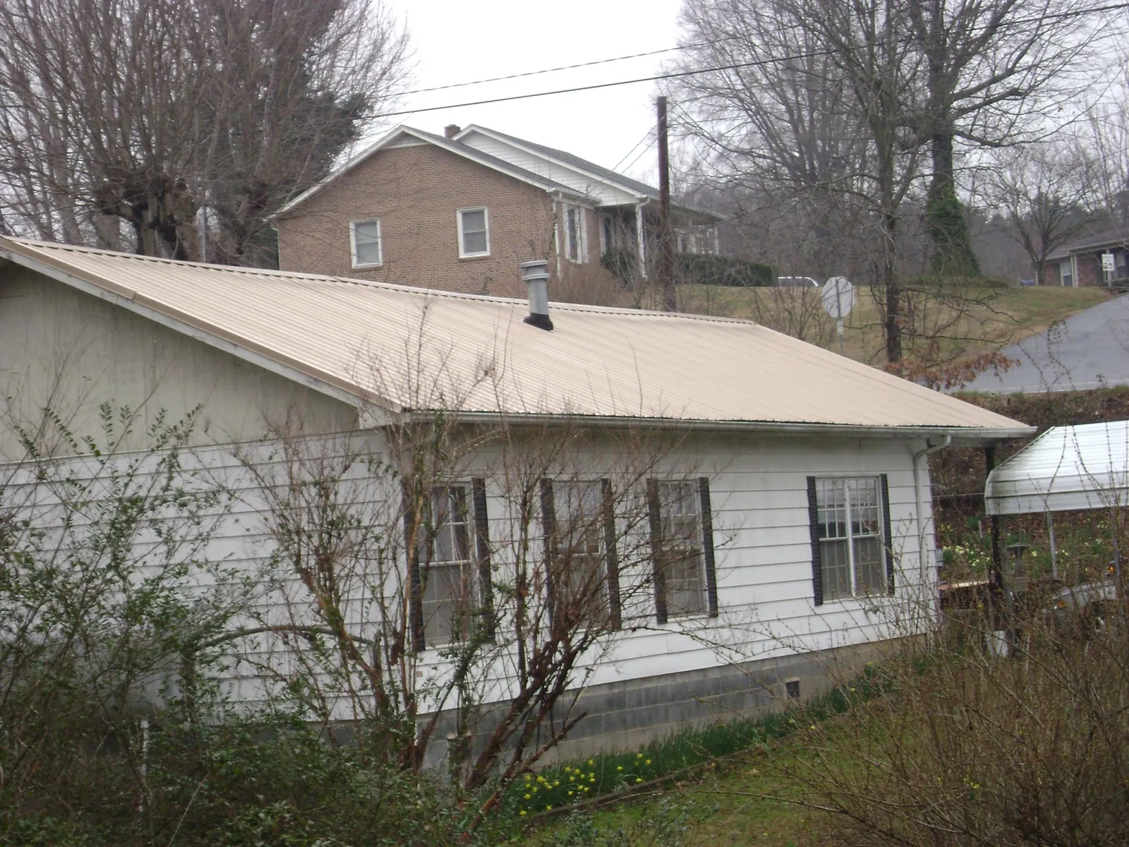 Tan metal roof on a white sided house set into a hillside — Commercial Roofing by Roofing Brothers in Marcellus