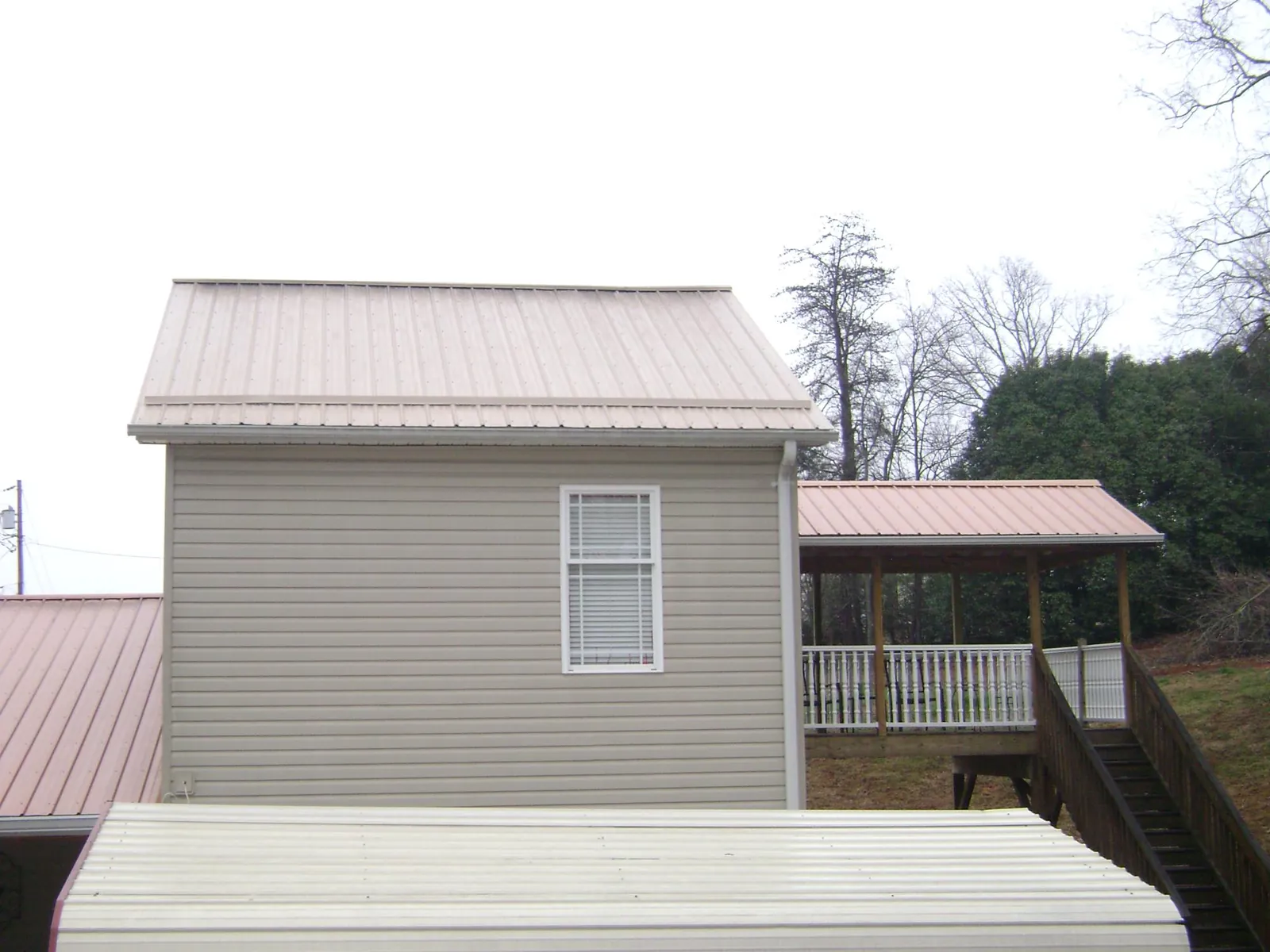 Tan metal roofs on a two story addition and attached porch, from a Roof Replacement job in Marcellus